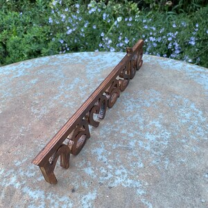 May include: A wooden sign with the word "Welcome" cut out in a decorative font. The sign is a warm brown color and is placed on a stone surface with a natural background of green foliage and blue flowers.