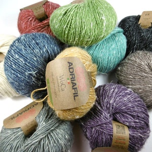 May include: Assortment of yarn skeins in various colours, including beige, green, blue, purple, grey, and brown. The yarn is a blend of wool and alpaca, and the skeins are labelled with the brand name "Adriafil" and the name "WoCa".