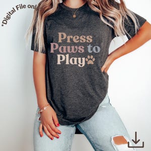 May include: Dark grey t-shirt with the text "Press Paws to Play" in a retro font. The design includes a paw print. The shirt is a digital file.