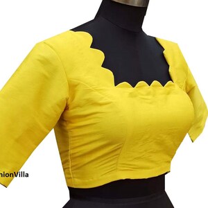Op de afbeelding: Een felgele blouse met korte mouwen en een gegolfde halslijn. De blouse is aangesloten en heeft een verkorte lengte.