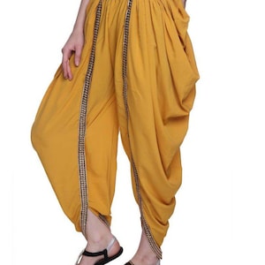 May include: Mustard yellow trousers with gold trim and a gathered design. The trousers are worn with black sandals.
