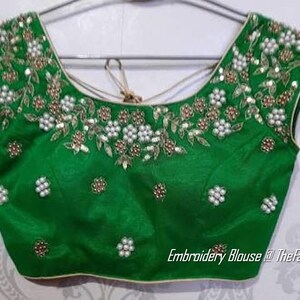 May include: A green embroidered blouse with white and gold embellishments. The blouse has a scoop neckline and short sleeves. The embroidery features pearls, sequins, and floral designs. The text "Embroidery Blouse @TheFashionVilla" is visible at the bottom of the image.