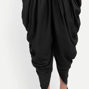May include: Black dhoti trousers with a gathered, pleated design. The trousers are made of a soft, flowing fabric and have a relaxed fit.