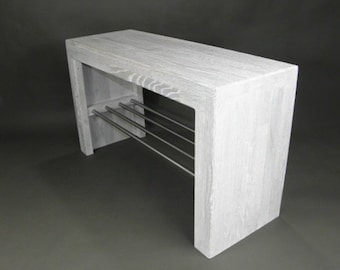Op de afbeelding: Witte houten schoenenbank met een metalen rek om schoenen op te bergen. De bank heeft een eenvoudig, modern ontwerp.