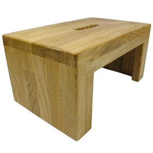K&ouml;nnte beinhalten: Ein helles Holztrittschemel mit rechteckiger Oberseite und einem ausgeschnittenen Griff. Der Hocker hat ein schlichtes, modernes Design mit einem stabilen Sockel. Die Holzmaserung ist sichtbar und verleiht ihm ein nat&uuml;rliches Aussehen.