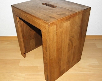 Könnte beinhalten: Ein Holzhocker mit rechteckiger Oberseite und einem Ausschnitt in der Mitte. Der Hocker ist aus hellbraunem Holz gefertigt und hat eine natürliche Oberfläche.