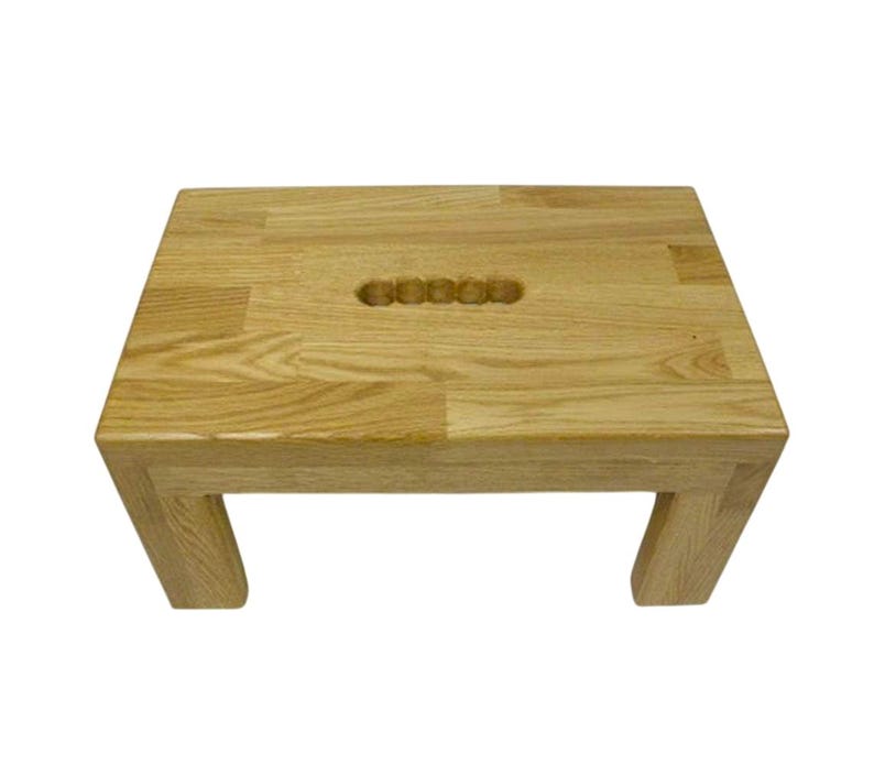 K&ouml;nnte beinhalten: Ein kleiner, rechteckiger Holzschemel mit nat&uuml;rlicher Oberfl&auml;che. Der Schemel hat einen eingelassenen Griff auf der Oberseite und vier stabile Beine. Die Holzmaserung ist im gesamten Schemel sichtbar.