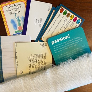 May include: A close-up of a variety of colorful index cards with handwritten text and illustrations. The cards are scattered on a wooden surface. The text on the cards includes "Islands in New York Harbor", "Lament", "passion!" and "The combination of sweet pineapple and slightly tart passion fruit is intensified by the tangy taste of kefir in this smoothie. It is a perfect antidote to a blah day, sip it morning, noon, or night."