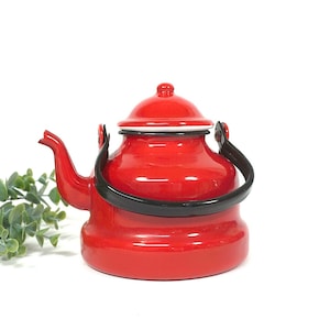 Op de afbeelding: Een helderrode emaille theepot met een zwarte handgreep en tuit. De theepot heeft een afgeronde body en een deksel met een kleine knop. De rand van het deksel is wit. Een klassiek keukenartikel.