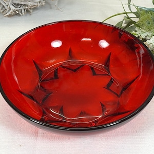 Könnte beinhalten: Eine rote Glasschüssel mit einem Sternmuster. Die Schüssel ist aus klarem Glas mit einer roten Tönung und hat einen schwarzen Rand.