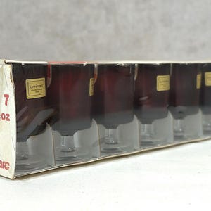 Peut inclure: Une boîte de six verres Luminarc en suède de 4 onces. Les verres sont transparents avec une teinte rouge foncé et portent une étiquette dorée indiquant "Luminarc".