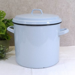 Könnte beinhalten: Ein großer, hellblauer Emaille-Kochtopf mit Deckel und seitlichen Griffen. Der Topf hat einen schwarzen Rand und einen kleinen Griff am Deckel. Der Topf ist zum Kochen und zur Zubereitung von Speisen bestimmt.