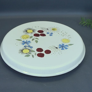 Puede incluir: Una bandeja redonda blanca con un diseño floral. La bandeja presenta un borde estriado y está decorada con flores amarillas, azules y rojas. Las flores están dispuestas en un patrón circular en la superficie de la bandeja.