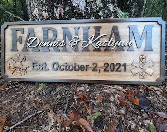 May include: A wooden sign with the last name "Farnham" and the names "Dennis & Katelyn" in cursive script. The sign also includes the text "Est. October 2, 2021" and two symbols, one representing a firefighter and the other a medical professional.