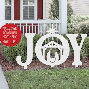 A red house with white trim. The front yard features a grass and pine straw surrounded bushes and a sidewalk. The SVG design shown is the word JOY spelled out with a nativity and star in the letter O. It is shown in white, placed in front of bushes.