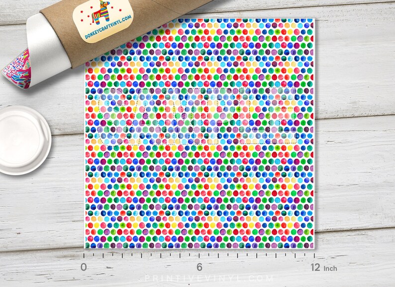 May include: A sheet of colorful vinyl with a repeating pattern of watercolor dots in various colors, including red, blue, green, and yellow. The sheet measures 12 inches wide. A roll of vinyl and a lid are in the background.