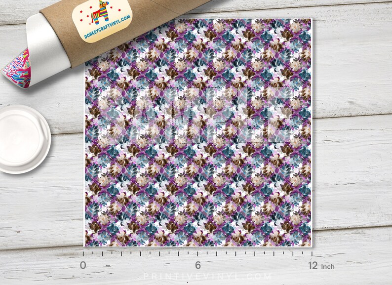 May include: A square sheet of patterned vinyl featuring a repeating floral design in shades of purple, teal, and brown on a white background. The sheet is approximately 12 inches wide. A roll of vinyl and a plate are in the image.