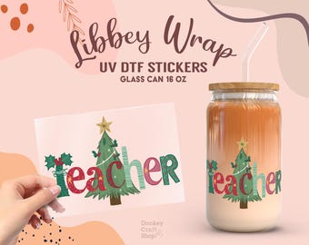May include: A clear glass can with a red and green Christmas tree and the word "Teacher" on it. The can is 473 ml and has a straw in it. The can is decorated with a UV DTF sticker.
