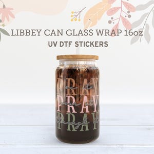 May include: A clear glass can with a wooden lid and a brown liquid inside. The can has a pink and green graphic that says "Pray on it Pray over it Pray through it".