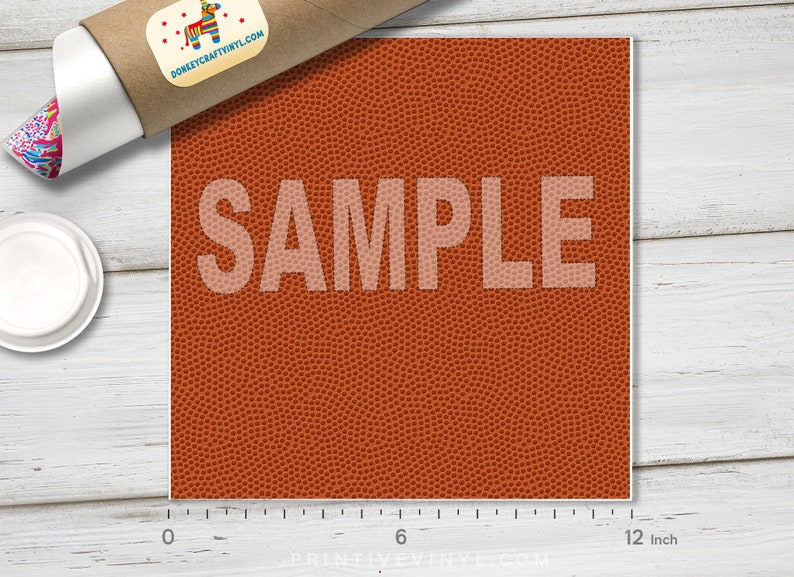 May include: A square sheet of orange vinyl with a basketball texture, measuring 12 inches across. The word "SAMPLE" is printed in a light color across the center. A rolled-up poster and a lid are in the background.