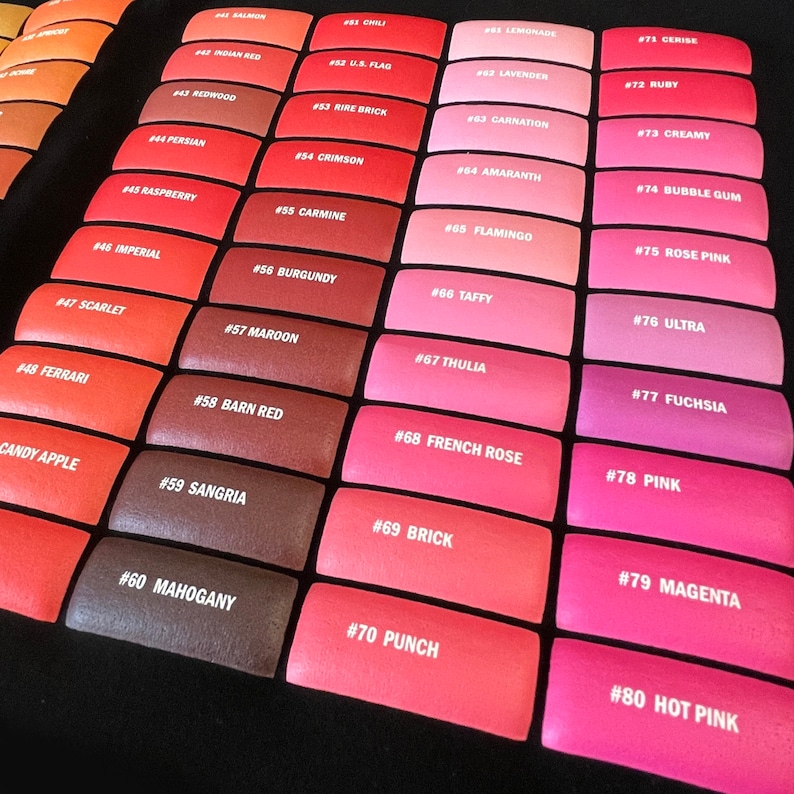 K&ouml;nnte beinhalten: Eine Farbkarte mit 80 verschiedenen Farbt&ouml;nen von rotem, rosa und orangefarbenem Lippenstift. Jede Farbe ist mit einer Nummer und einem beschreibenden Namen gekennzeichnet, wie z. B. "Kirsche", "Rubin" und "Pink".