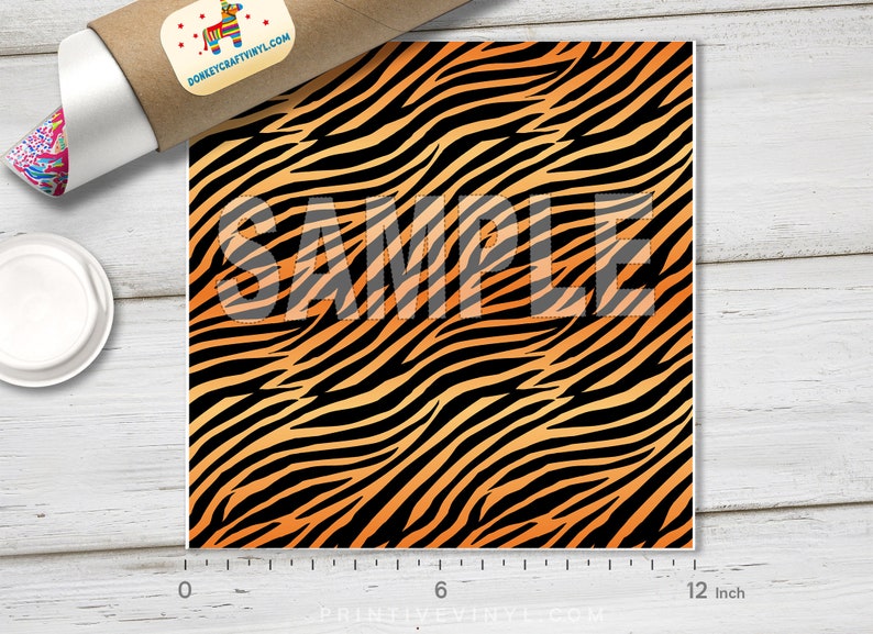 May include: A 12-inch by 12-inch sheet of orange and black tiger stripe vinyl. The vinyl has a gradient effect, with the orange being lighter at the top and darker at the bottom. The vinyl is marked "SAMPLE" in the center.