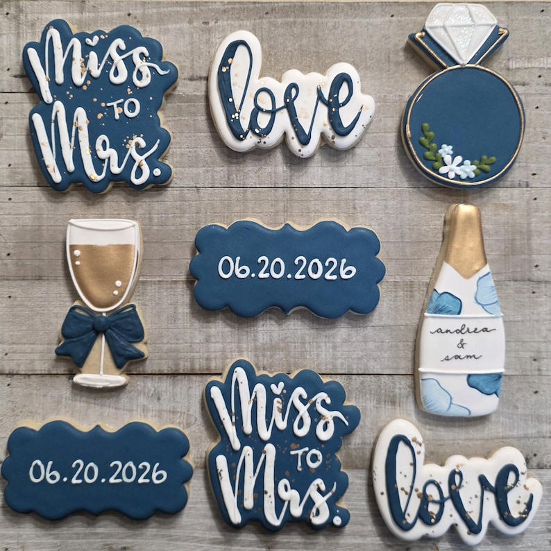 K&ouml;nnte beinhalten: Eine Auswahl an dekorierten Keksen mit Hochzeitsthema. Designs beinhalten die W&ouml;rter "Miss to Mrs.", "Love", einen Diamantring, eine Champagnerflasche, ein Champagnerglas und das Datum "06.20.2026". Die Kekse sind mit blauer, wei&szlig;er und goldener Glasur verziert.