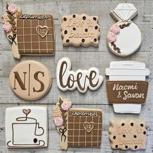 May include: Assortment of decorated cookies with a wedding theme. Cookies include a calendar with "September 12", a diamond ring, a coffee cup, and cookies with the words "love is brewing". Some cookies have initials and floral accents.