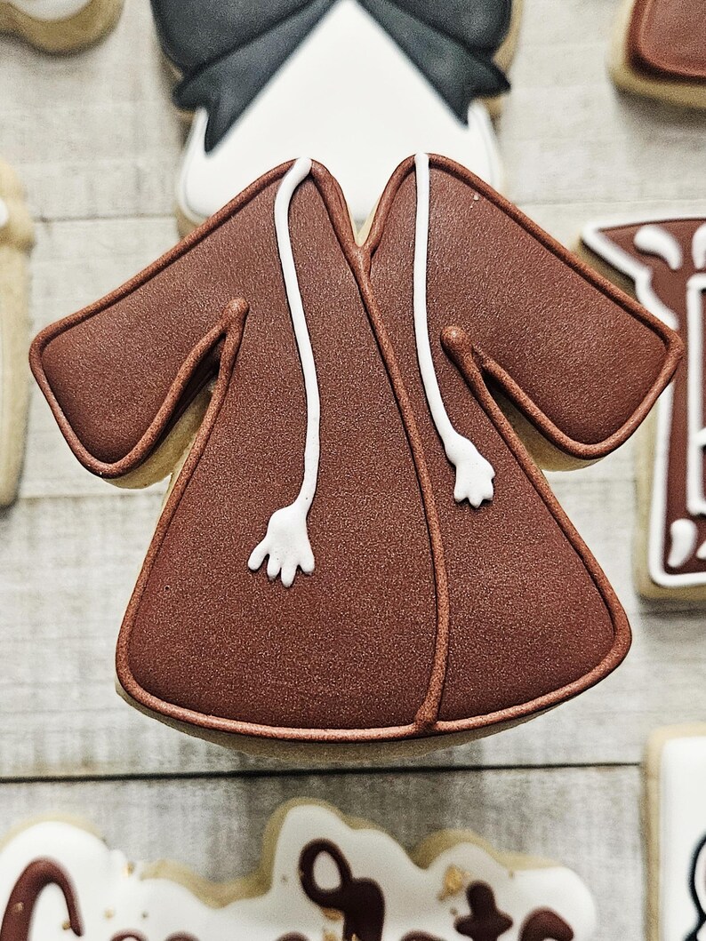 May include: A brown sugar cookie decorated with white icing to look like a robe. The robe has a white hood and two white cords.
