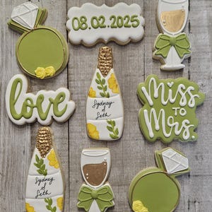 K&ouml;nnte beinhalten: Auswahl an dekorierten Zuckerkeksen mit Hochzeitsthema. Die Kekse umfassen einen Diamantring, eine Champagnerflasche, ein Champagnerglas und Kekse mit den Schriftz&uuml;gen "love", "Miss to Mrs." und dem Datum "08.02.2025". Die Kekse sind mit gr&uuml;ner, wei&szlig;er und goldener Glasur verziert.