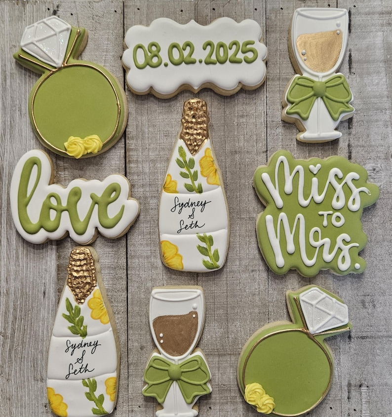 K&ouml;nnte beinhalten: Auswahl an dekorierten Zuckerkeksen mit Hochzeitsthema. Die Kekse umfassen einen Diamantring, eine Champagnerflasche, ein Champagnerglas und Kekse mit den Schriftz&uuml;gen "love", "Miss to Mrs." und dem Datum "08.02.2025". Die Kekse sind mit gr&uuml;ner, wei&szlig;er und goldener Glasur verziert.