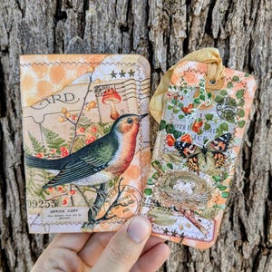 May include: A rectangular card and a vertical tag featuring collage-style artwork. The card displays a bird on a branch with vintage postal stamps and text. The tag features a butterfly, a bird's nest with eggs, and a yellow ribbon tie.