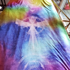 Puede incluir: Una manta de forro polar colorida con un diseño geométrico blanco. La manta presenta un degradado arcoíris de rosa, morado, azul, verde y amarillo.