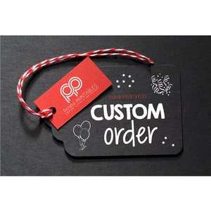 Puede incluir: Una etiqueta de pizarra negra con texto blanco que dice "CUSTOM order" y una pequeña ilustración de globos. La etiqueta está atada con un cordel de panadero rojo y blanco a una etiqueta roja con el logotipo "PP" y el texto "PANINI PRINTABLES CUSTOM SIGNS & INVITATIONS".
