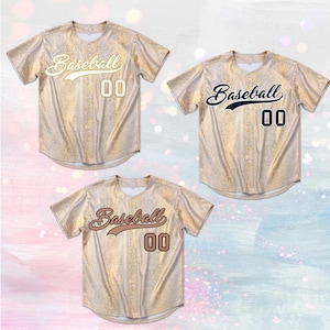 Op de afbeelding: Drie honkbalshirts met een gouden glitterontwerp. Elk shirt heeft het woord "Baseball" in script en het nummer "00". De kleuren van het script en het nummer zijn wit, marineblauw en bruin.