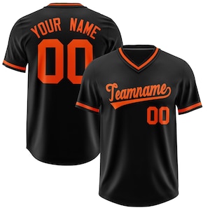 May include: Black baseball jersey with orange trim and lettering. The back of the jersey says "YOUR NAME" and has the number "00". The front of the jersey says "Teamname" and has the number "00".