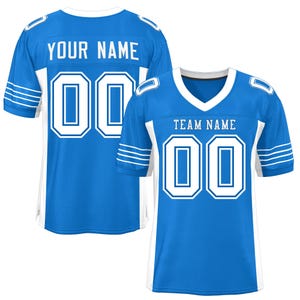 May include: A blue and white football jersey with white stripes on the sleeves. The jersey has a white v-neck collar and white numbers on the front and back. The text "YOUR NAME" is on the back of the jersey and "TEAM NAME" is on the front.