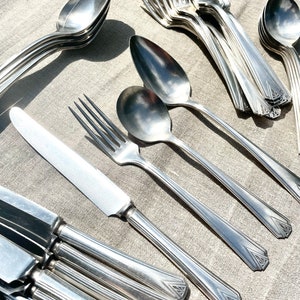 Puede incluir: Un juego de cubiertos vintage, que incluye tenedores, cucharas y cuchillos, todos con un acabado plateado pulido. Los cubiertos tienen un diseño Art Deco con patrones geométricos en los mangos.
