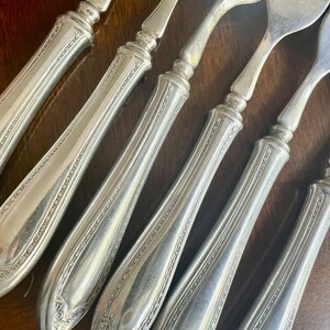 May include: Six silver forks with ornate handles. The forks have a decorative pattern on the handles and are arranged in a row.