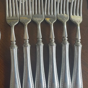 May include: A set of six silver forks with ornate handles. The forks have a traditional design with a rounded handle and a three-pronged head.