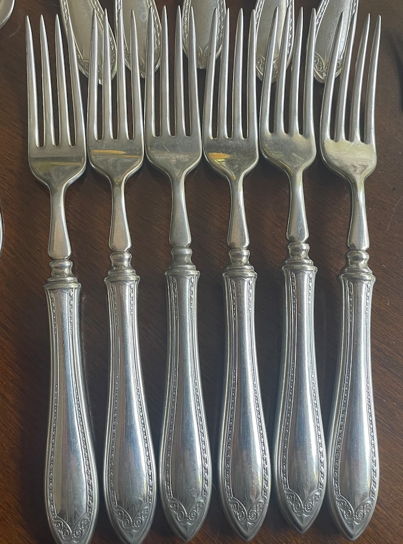 May include: A set of six silver forks with ornate handles. The forks have a traditional design with a rounded handle and a three-pronged head.