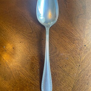May include: A silver spoon with an ornate design on the handle. The spoon is polished and shiny.