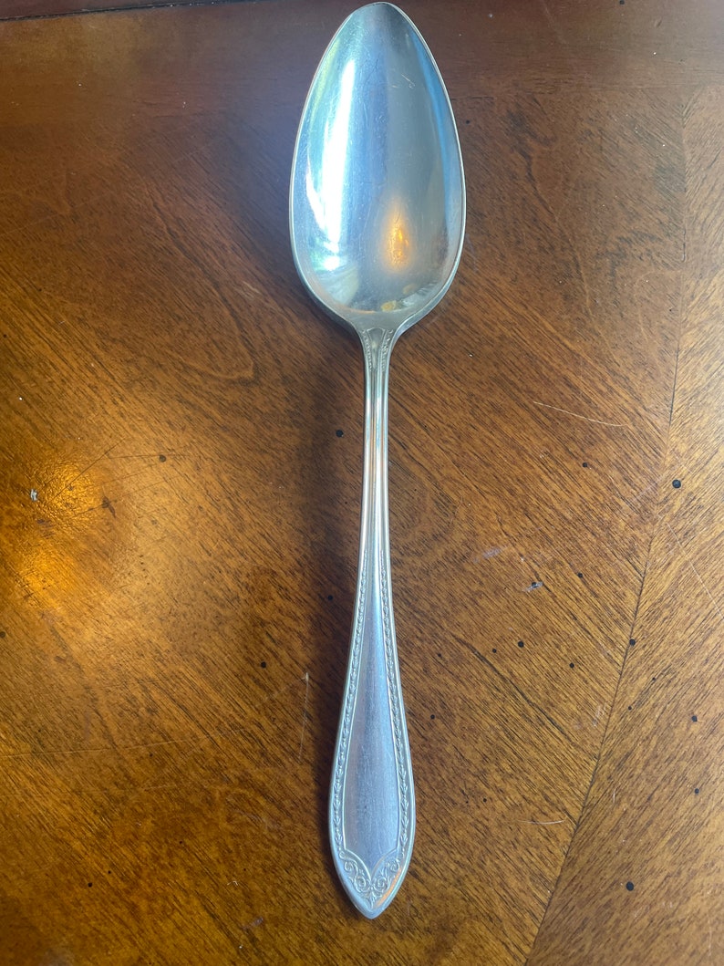 May include: A silver spoon with an ornate design on the handle. The spoon is polished and shiny.