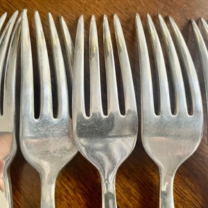 May include: Close-up of a set of six silver forks, showing the tines and polished surface.