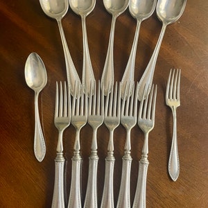 May include: A set of eight silver-plated utensils, including six forks and two spoons. The forks have ornate handles with a decorative pattern. The spoons have a similar pattern on the handles.