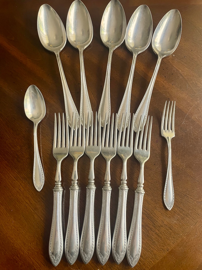 May include: A set of eight silver-plated utensils, including six forks and two spoons. The forks have ornate handles with a decorative pattern. The spoons have a similar pattern on the handles.