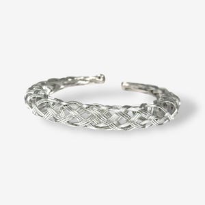 May include: A silver-colored open cuff bracelet. The bracelet features a woven design, with multiple strands of metal intertwined to create a textured appearance. The ends of the bracelet are open, allowing for easy adjustment and wear.