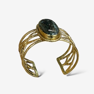 May include: A gold-toned bangle bracelet with a delicate, intricate design. The bracelet features a large, oval-shaped, dark green gemstone set in a gold bezel.