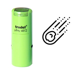 May include: A light green Trodat printy 4612 stamp with a black comet graphic. The stamp has a rectangular design with rounded edges and a clear top. The comet graphic is a black outline of a celestial object with a tail of lines and dots.