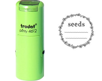 以下が含まれることがあります： 「trodat printy 4612」というテキストと、円形のスタンプデザインに「seeds」というテキストと花の装飾的な境界線が付いた緑色の自動インクスタンプです。